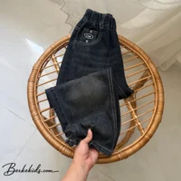 شلوار جین بچگانه پسرانه رنگ گازوئیلی تا شده روی صندلی حصیری
