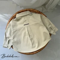 پیراهن پسرانه اسپرت بچگانه چیده شده روی صندلی حصیری برای نمایش فرم لباس